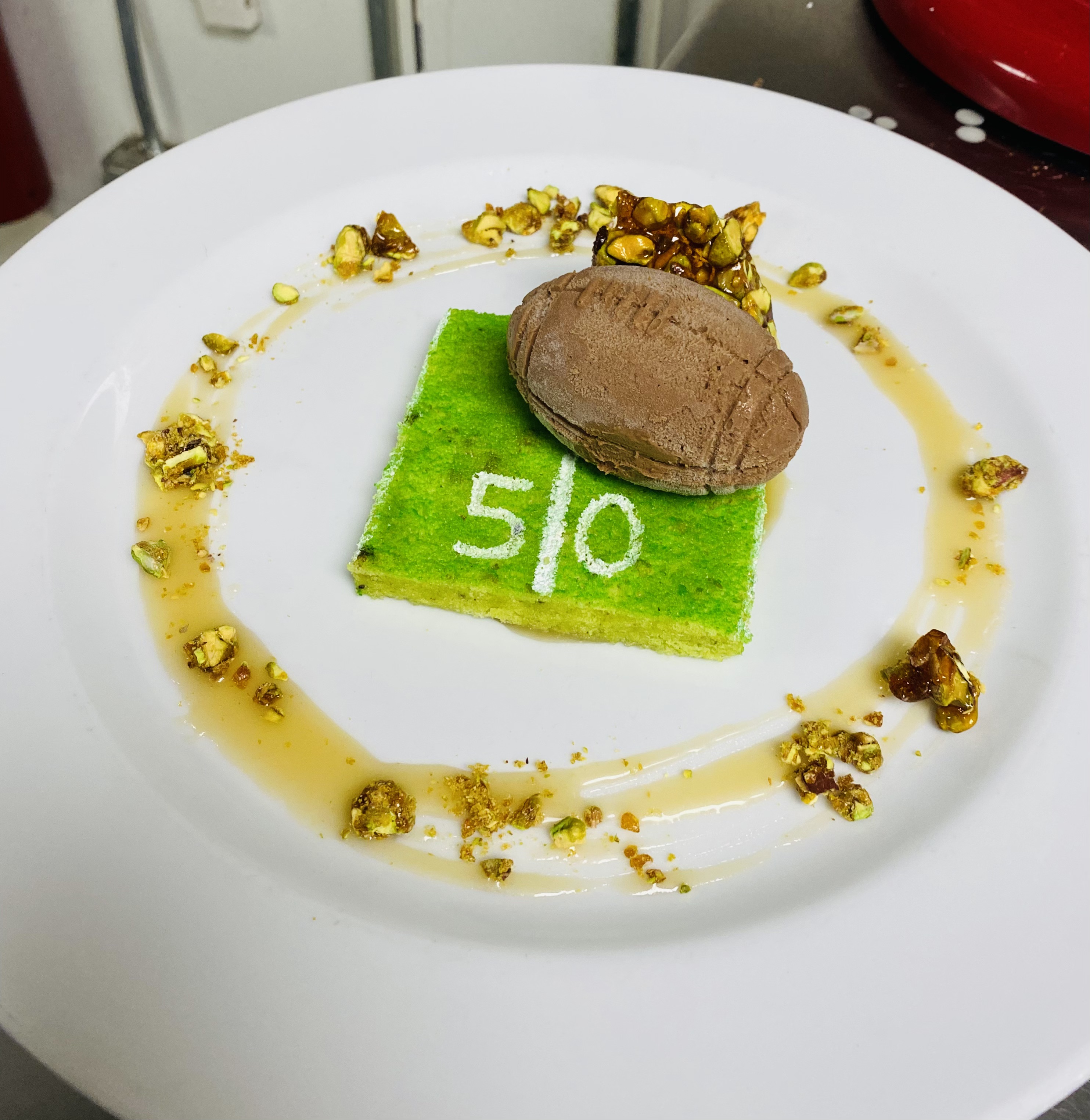 Plated pistachio sponge with chocolate quenelle dessert